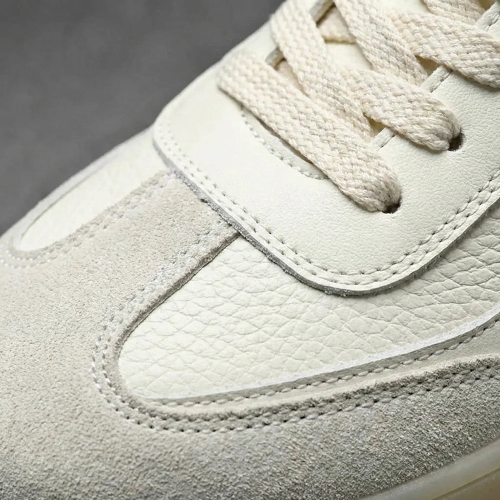 Close-up of the beige trainer's toe box showing stitched suede and leather panels with cream laces.