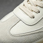 Close-up of the beige trainer's toe box showing stitched suede and leather panels with cream laces.