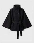 Product shot of the black belted cape jacket laid flat, showing button stand collar and wide bell sleeves