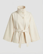 Cream belted cape jacket laid flat, highlighting the tall stand collar and self-tie waist belt