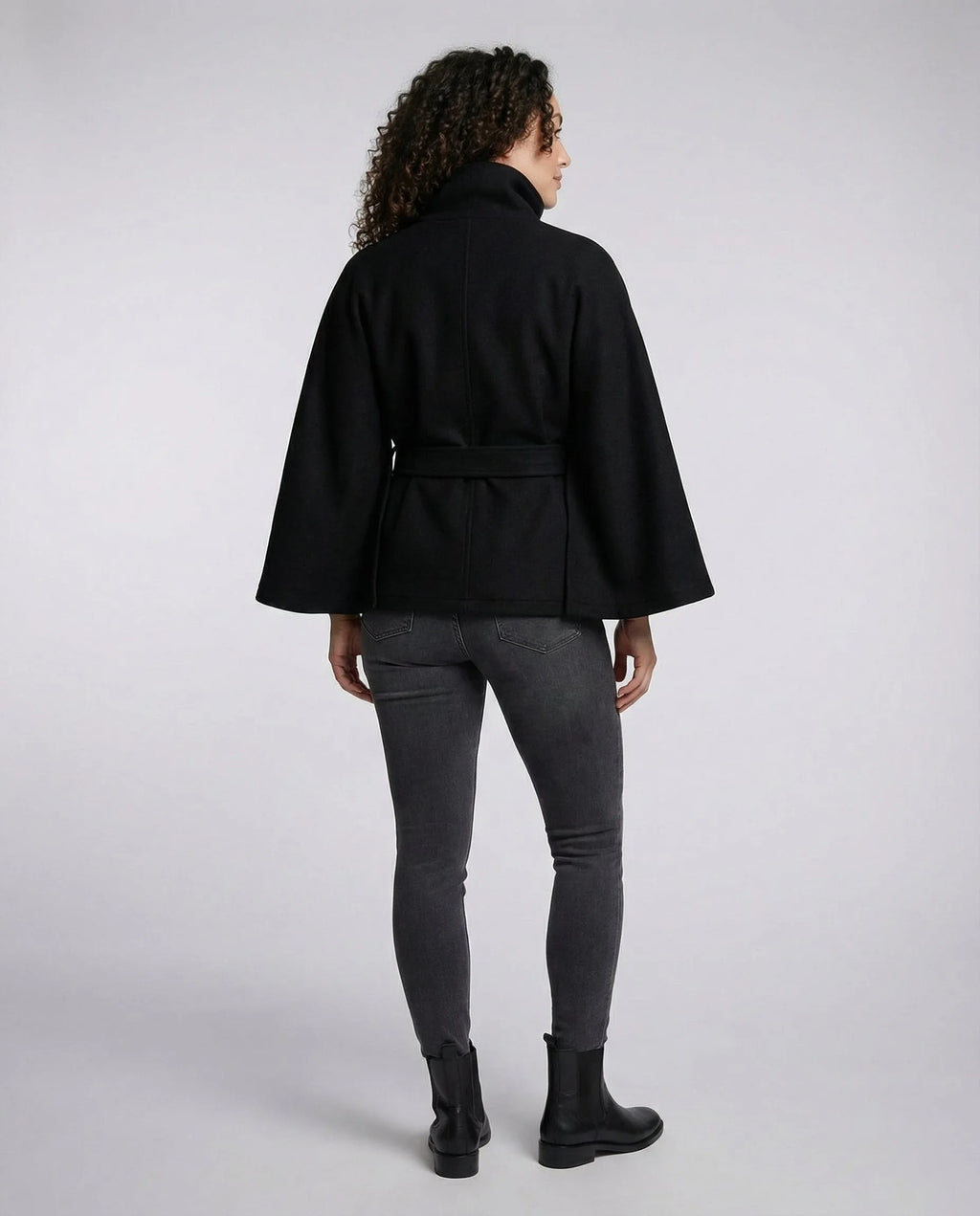 Back view of the black belted cape coat, showing the rear seam detail and relaxed sleeve drape