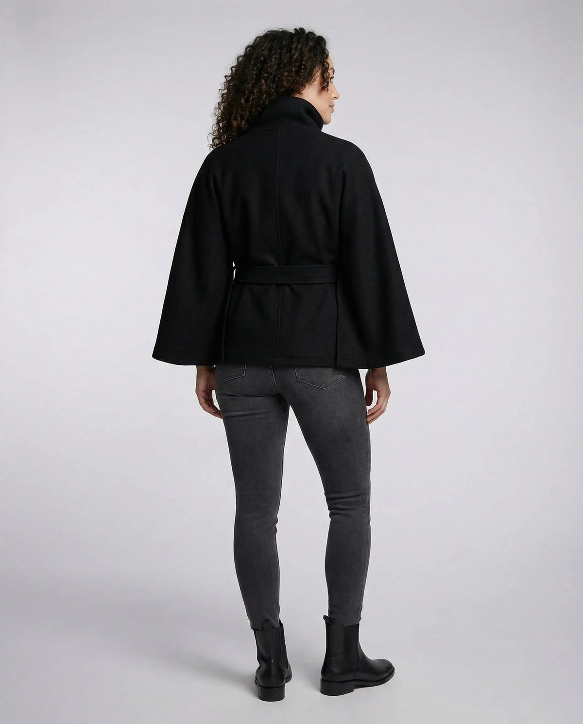 Back view of the black belted cape coat, showing the rear seam detail and relaxed sleeve drape