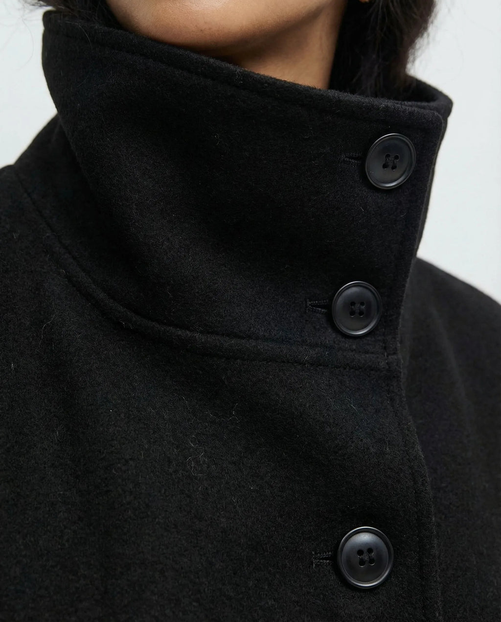 Close front view of the black cape jacket on a model, highlighting the buttoned stand collar and tied belt