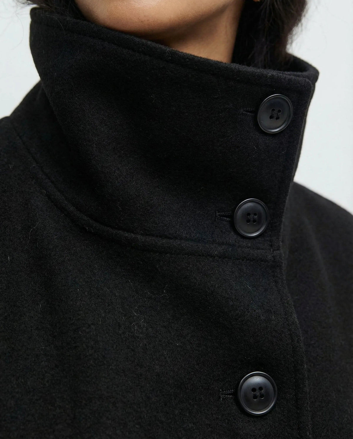 Close front view of the black cape jacket on a model, highlighting the buttoned stand collar and tied belt