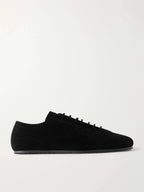 Side profile of a black suede lace-up sneaker with a rounded toe and thin flat sole on a plain background.