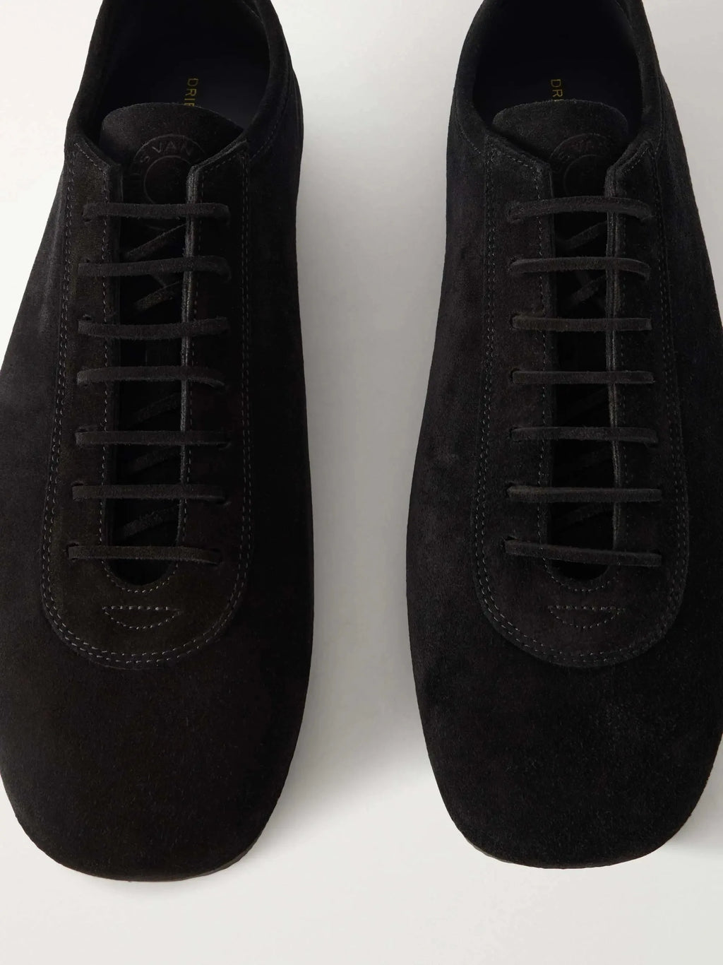 Top-down view of a pair of black suede sneakers showing the lacing detail and branded heel tab.