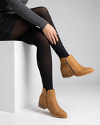 Close-up side view of tan faux-leather ankle boots with side zip and stacked block heel, worn with black tights