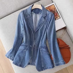 Blue denim blazer hanging on a cream hanger, showing its flared peplum hem and front welt pockets styled beside a tote bag