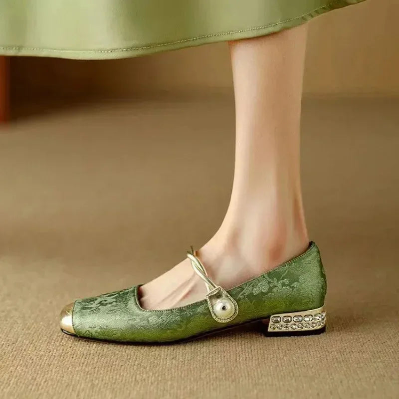 Side profile of a green floral brocade flat worn on the foot, showing the crystal-studded low block heel