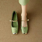 Top-down view of a pair of green brocade Mary Jane flats with twisted gold pearl straps and matching insoles