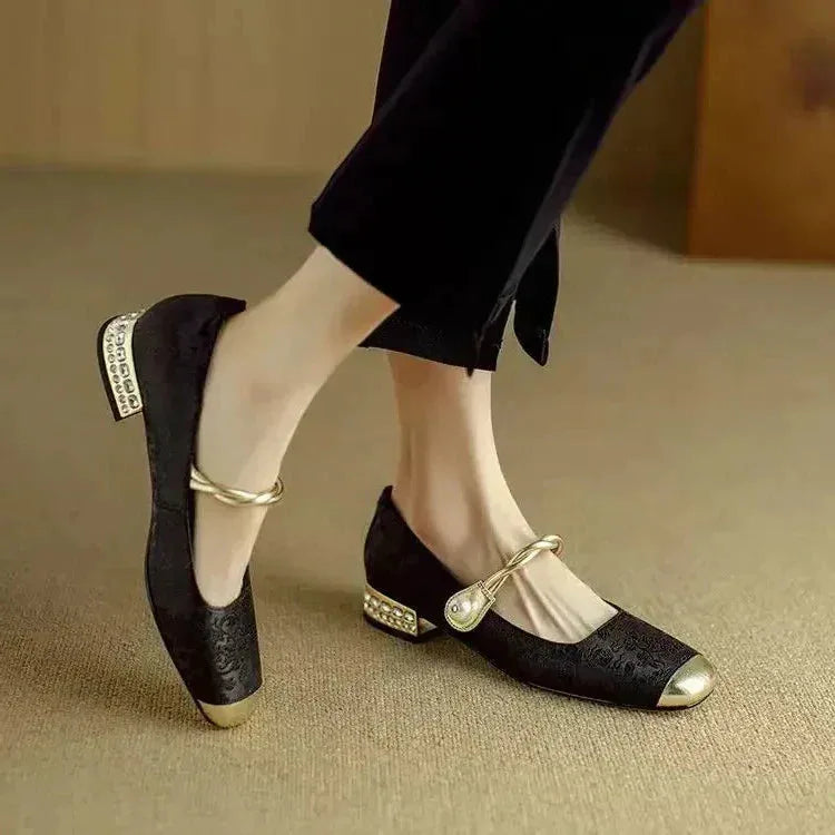 Side view of a black floral brocade flat with gold metallic toe and jewelled block heel