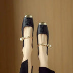 Top-down view of black brocade Mary Jane flats worn on both feet with gold twisted straps
