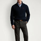 Man wearing a navy cable-knit quarter-zip jumper over a light blue shirt with grey trousers and a brown belt