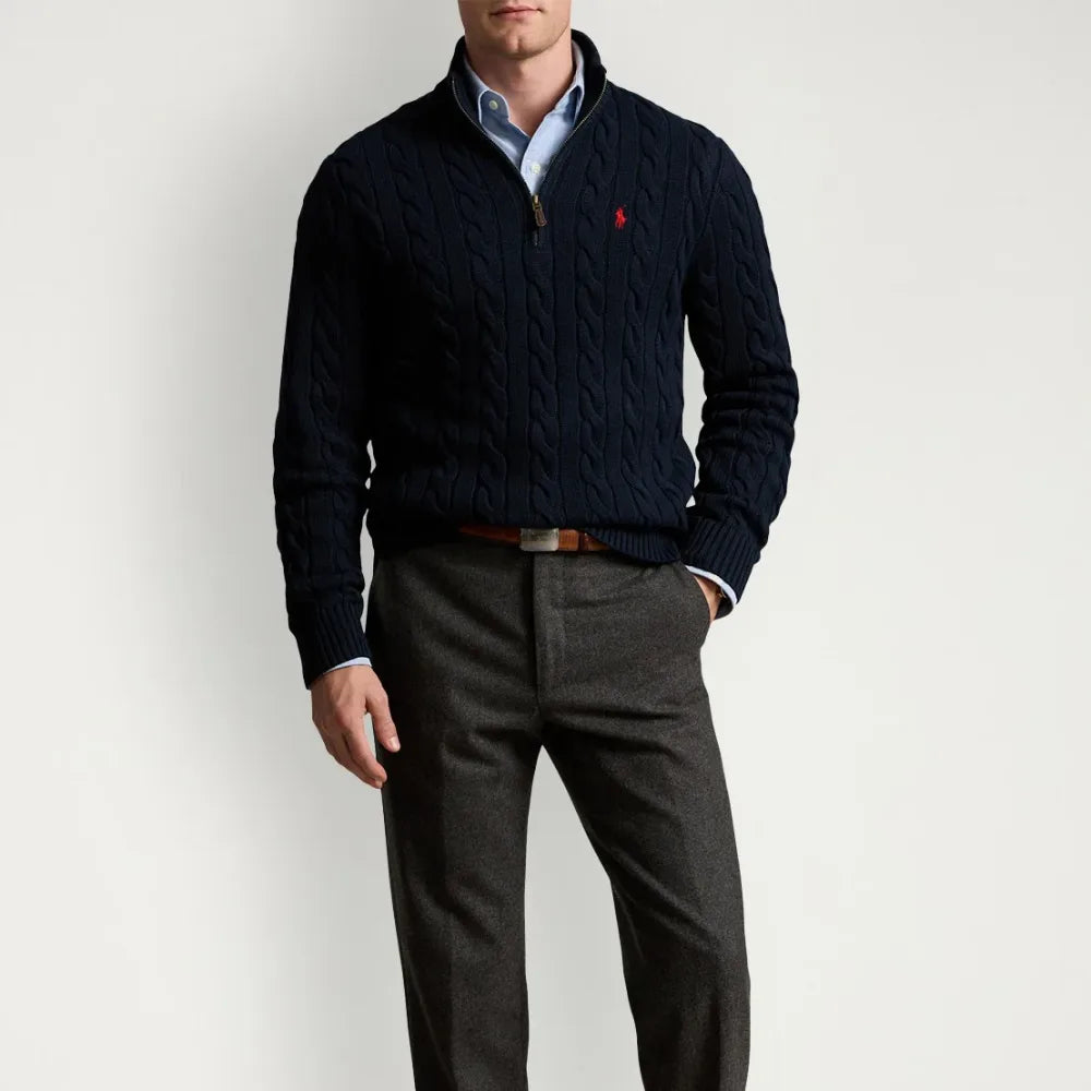 Man wearing a navy cable-knit quarter-zip jumper over a light blue shirt with grey trousers and a brown belt