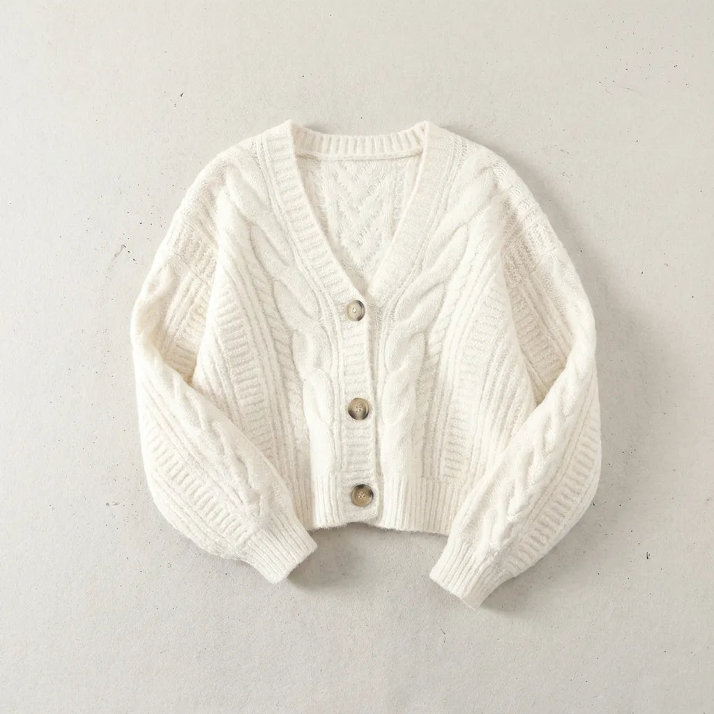 Cream white cable-knit cropped cardigan with three horn-style buttons, laid flat on a neutral backdrop
