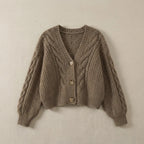 Taupe brown cable-knit cropped cardigan with ribbed cuffs and V-neckline, laid flat on a textured surface