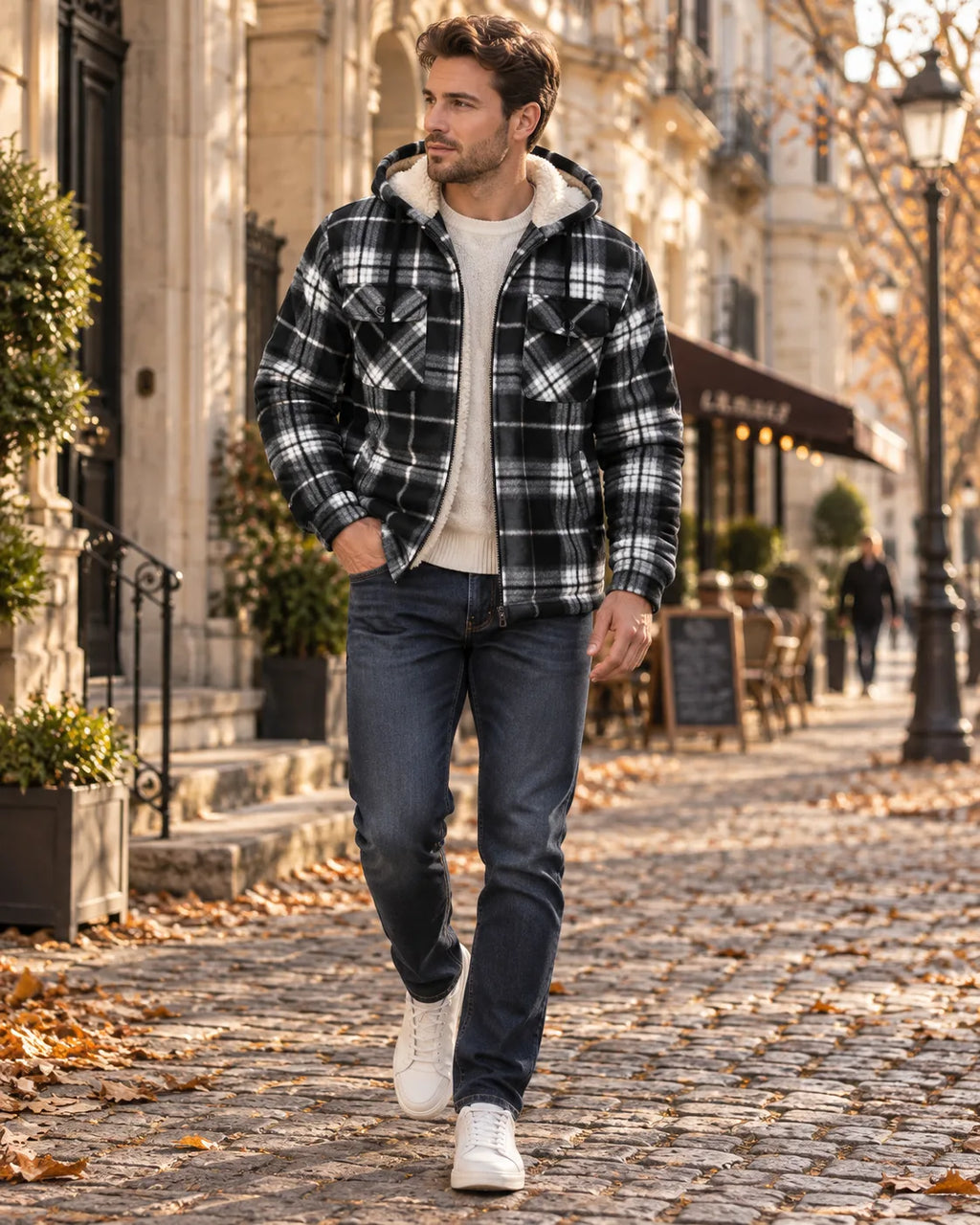 Man wearing a black and white checked hooded jacket with sherpa lining over a cream jumper and dark jeans on a cobbled street