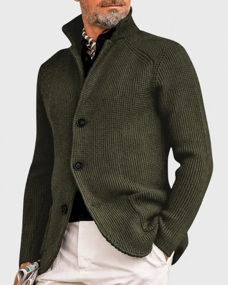 Side view of olive green chunky knit cardigan with stand collar and button front, worn over a dark shirt and scarf
