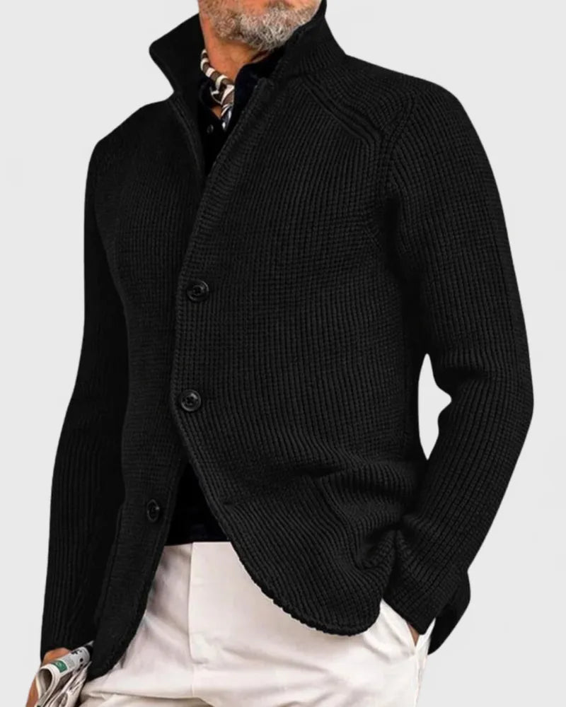 Black chunky knit cardigan with high stand collar and three-button front, paired with white trousers