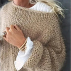 Close-up of the ribbed cuff and loose knit texture on a beige chunky jumper, worn over a white blouse
