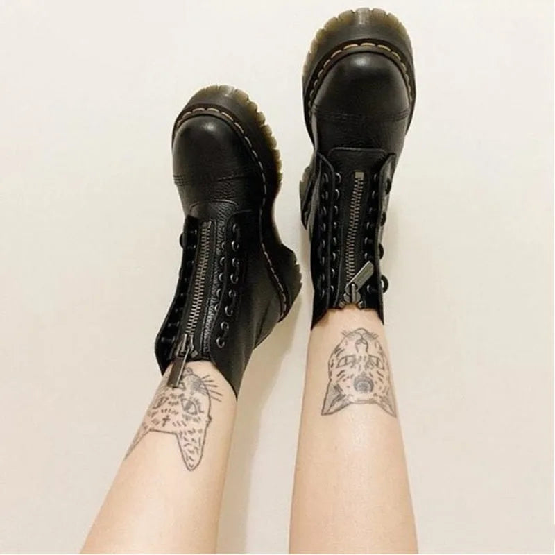 Close-up of raised legs wearing black pebbled leather platform boots with front zip and lace detailing against a plain wall