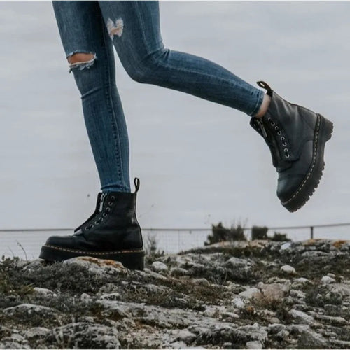 Side profile of a model stepping forward in black chunky platform boots paired with ripped skinny jeans outdoors