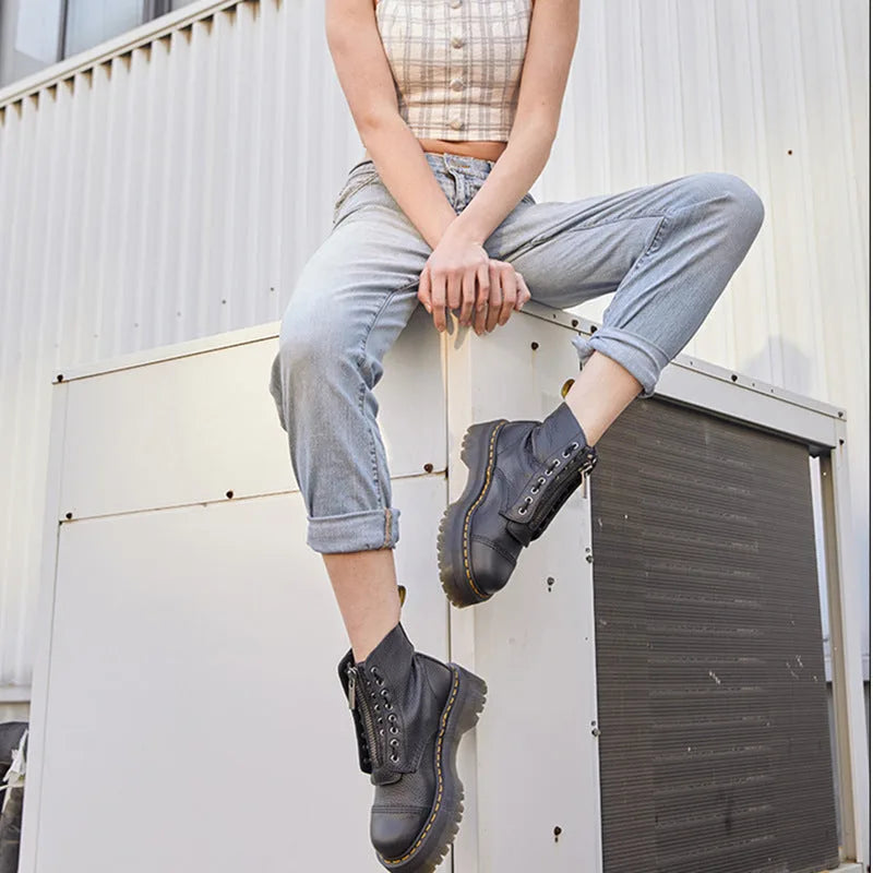Woman sitting with legs crossed, wearing black platform boots with turned-up light denim jeans