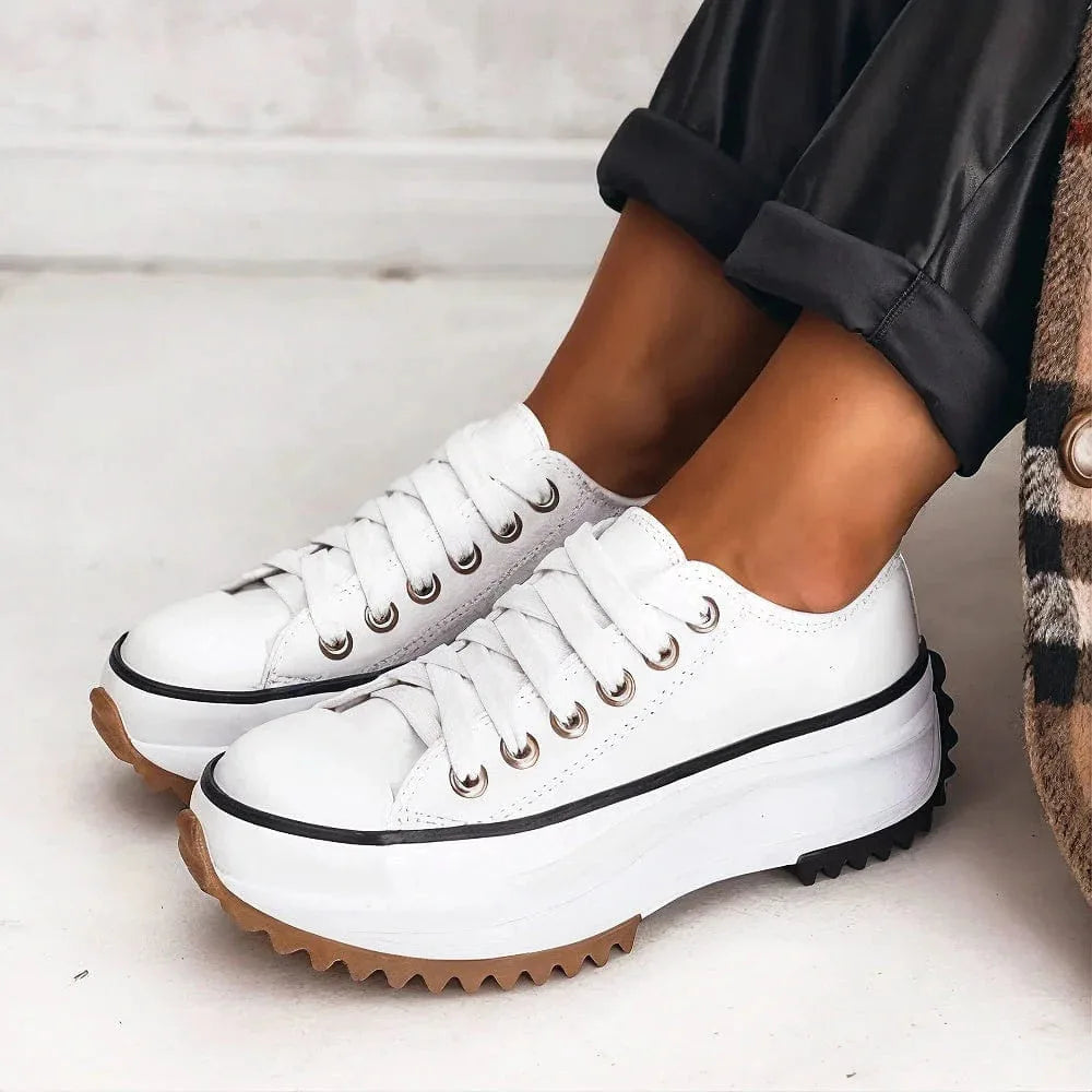 Close-up of white leather lace-up platform trainer with black trim and gum-coloured ridged sole.