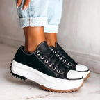 Black canvas platform trainer with white toe cap, white stitching and thick tread sole shown from the side.