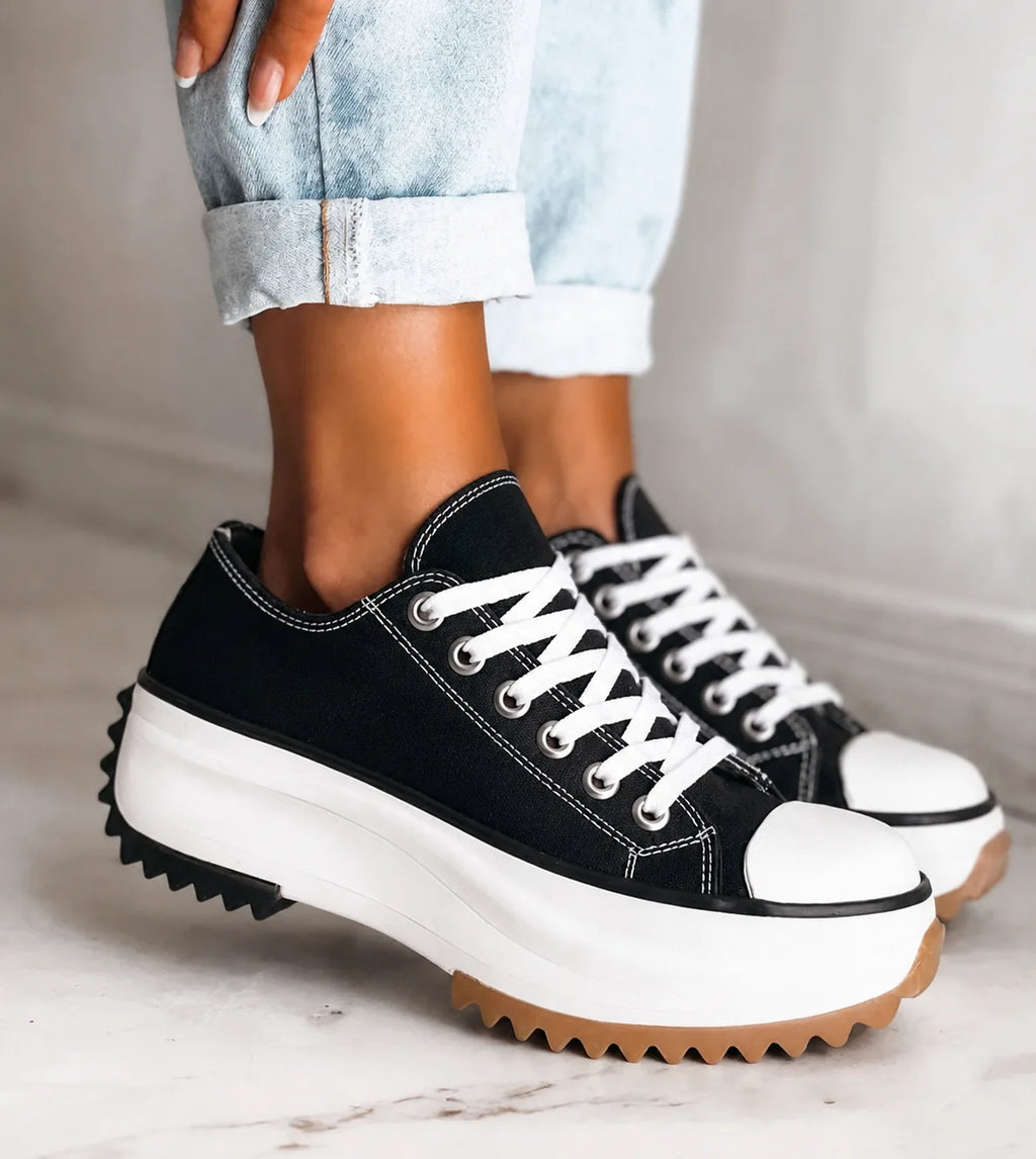 Black canvas trainers with white laces and toe caps, chunky white platform sole with gum tread, worn with rolled-up jeans.