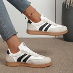 Side view of white trainer with black stripes and suede toe panel, worn on foot with beaded anklet