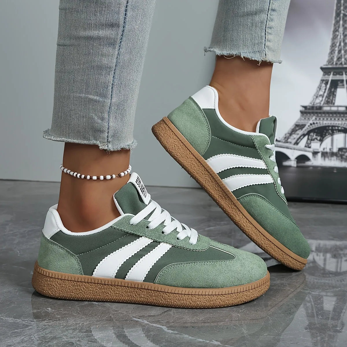 Close-up side profile of sage green trainer with white stripes and gum rubber sole
