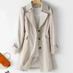 Cream trench coat on a wooden hanger, single-breasted with wide lapels and tortoiseshell buttons over a white t-shirt