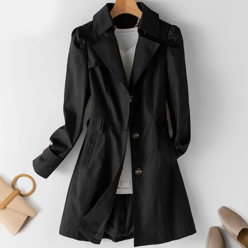 Black single-breasted trench coat with puffed shoulders and flap pockets, paired with a white top and beige mules
