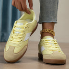 Close-up of hand lacing a yellow trainer with star logo tongue, suede toe panel and contrasting gum sole