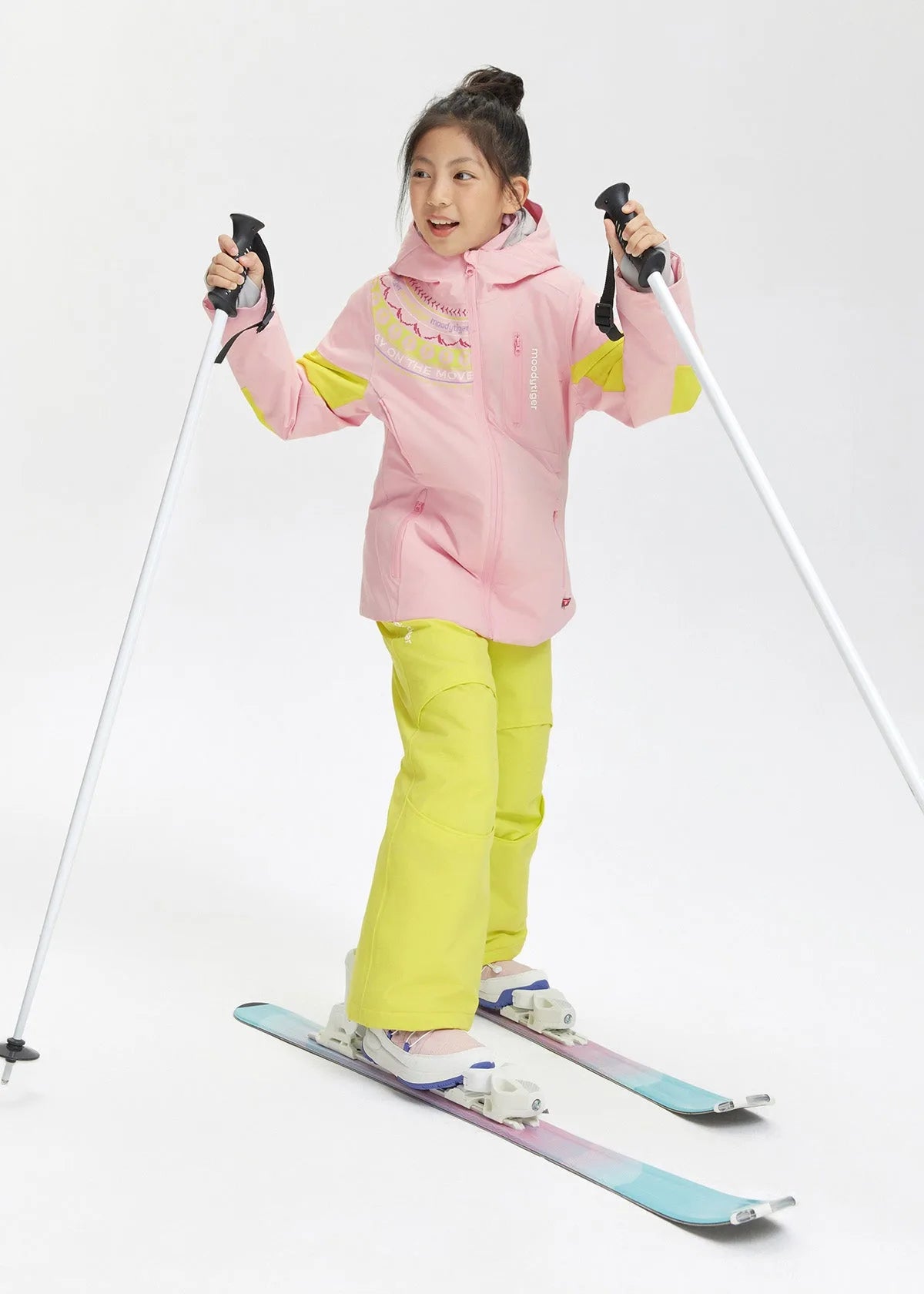 Front view of a girl wearing a pink hooded ski jacket with yellow sleeve panels, holding ski poles
