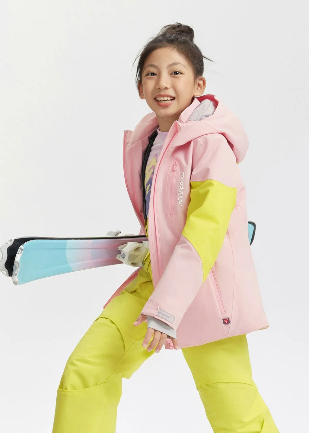 Girl smiling while holding skis, showing the fitted hood and zip chest pocket of the pink jacket