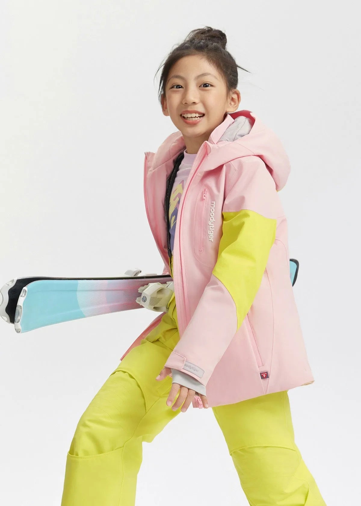 Girl smiling while holding skis, showing the fitted hood and zip chest pocket of the pink jacket