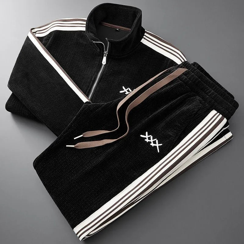 Black corduroy zip-up jacket and matching joggers folded together, showing brown and cream side stripes and drawstring waist