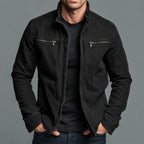Man wearing a faded black cotton zip jacket with stand collar and twin chest zip pockets, hands in pockets