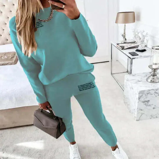 Woman wearing a sea blue crew neck loungewear set with printed text detail on the trouser leg, paired with white trainers