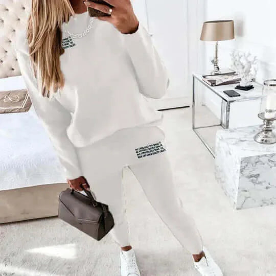 White two-piece loungewear set with long sleeve top and jogger trousers, shown from behind in a bright bedroom setting