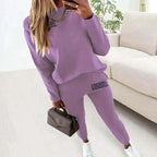 Purple loungewear set with relaxed fit sweatshirt and matching joggers, styled with a grey handbag and white trainers