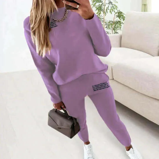 Purple loungewear set with relaxed fit sweatshirt and matching joggers, styled with a grey handbag and white trainers