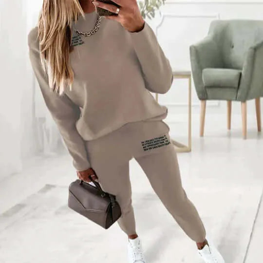 Khaki loungewear set with crew neck top and elastic waist joggers, worn with white trainers in a cosy living room