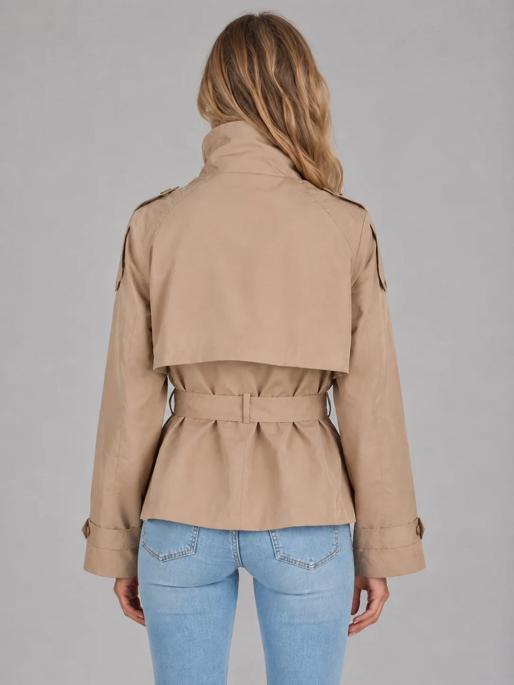 Back view showing the cropped hem, storm flap detail and belted waist of the beige double-breasted jacket