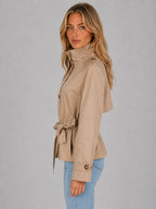 Side profile highlighting the stand collar, tied belt bow and structured shoulder of the beige trench jacket
