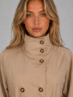 Close-up of the stand collar and double-breasted tortoiseshell buttons on the beige woven jacket fabric