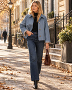 Woman in a dusty blue short jacket with gingham-lined cuffs, black polo neck and wide-leg jeans, walking a Parisian street