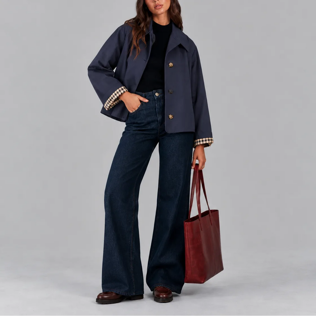 Front view of a navy cropped trench jacket buttoned up, styled with dark wide-leg denim